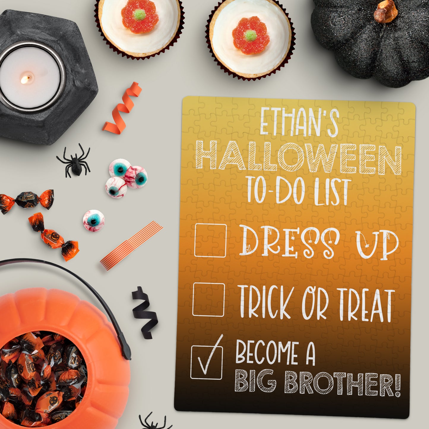 A Halloween-themed flat lay with candy, decor, and a puzzle announcing āEthanās Halloween To-Do List: Dress Up, Trick or Treat, Become a Big Brother!ā.