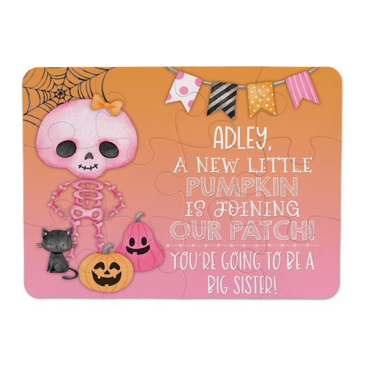 A pink skeleton with a bow stands next to pumpkins, a black cat, and a banner. The text says a new pumpkin is joining the patch and announces a girl will be a big sister.