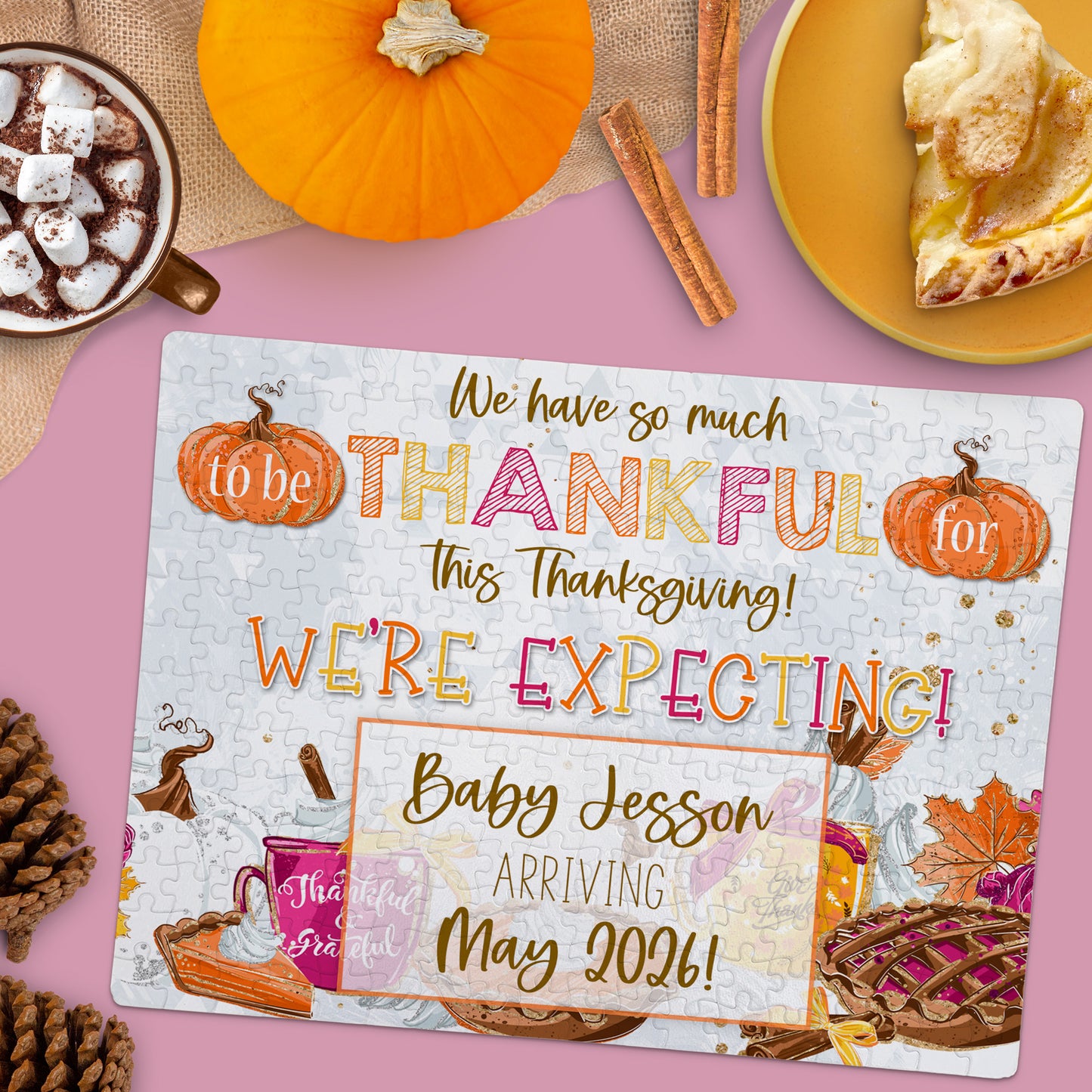 A jigsaw puzzle on a table announces a pregnancy with the text, “We're expecting! Baby Jesson arriving May 2026,” surrounded by fall decor, pie, and hot chocolate.